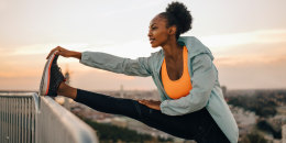 Sportswoman doing stretching exercise against sky during sunset