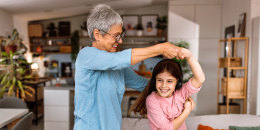 Happy active grandmother dancing with her granddaughter at home. Holding hands, dancing and jumping to the music. Family fun.