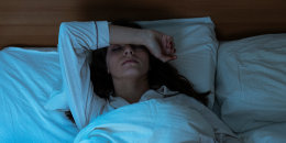 Woman in bed covering eyes with hands.